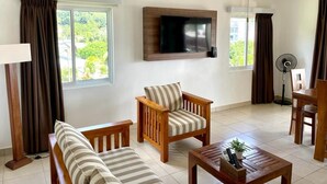 A living room with a sofa, armchair, and coffee table. There is a TV mounted on the wall and a fan in the corner. - Tropical Hideaway (Mahé Island)