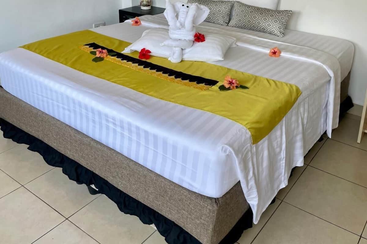 A neatly made bed with a yellow and white bedspread, a mirror above it, and a small bedside table with a lamp.