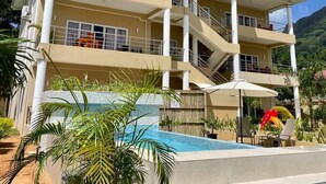 A multi-story hotel with a pool area, outdoor seating, and a mountain backdrop. - Tropical Hideaway (Mahé Island)