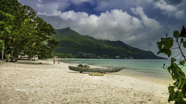 A beach with a boat, clear water, and a mountain in the background. - Tropical Hideaway (Mahé Island)