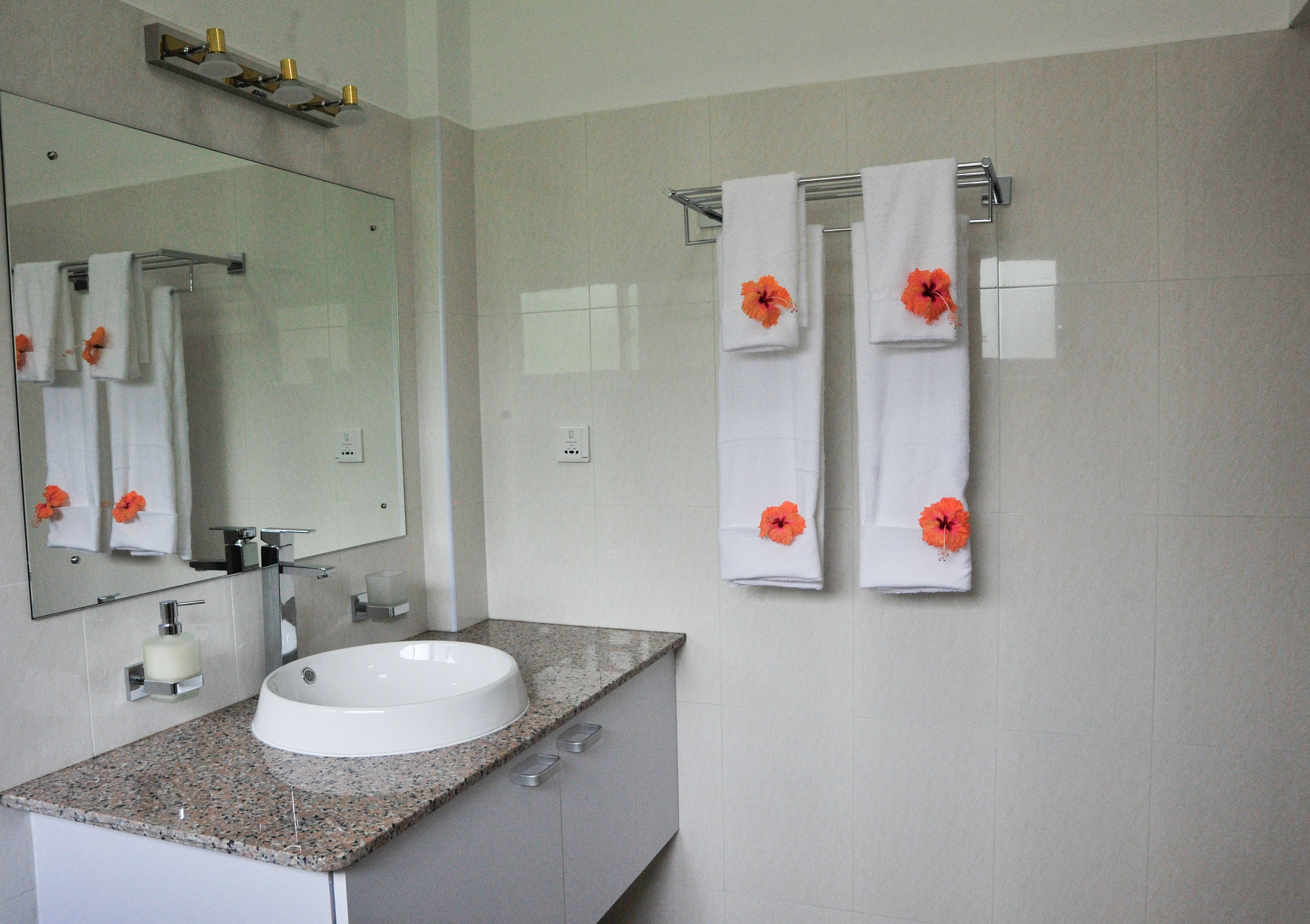 Une salle de bain avec un lavabo blanc, un miroir et deux serviettes ornées de motifs floraux orange.