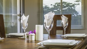 A dining table set with white plates, silverware, and folded napkins in clear glassware, with a candle and a small vase of purple flowers. - Tropical Hideaway (Mahé Island)