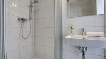 A modern bathroom with a glass-enclosed shower, a white sink with a vase of flowers, and a mirror above the sink.