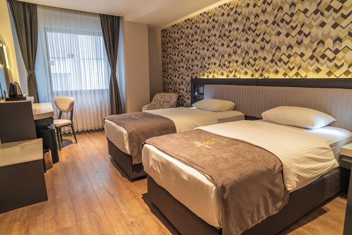 A hotel room with two beds, a desk, a chair, and a patterned wall.