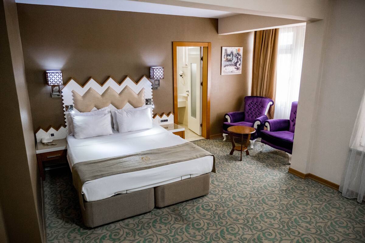 A hotel room with a large bed, a chair, a small table, and a door leading to a bathroom.