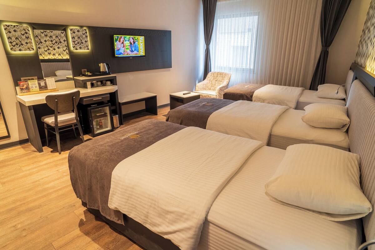 A hotel room with a TV, desk, chair, two beds, and a window with curtains.