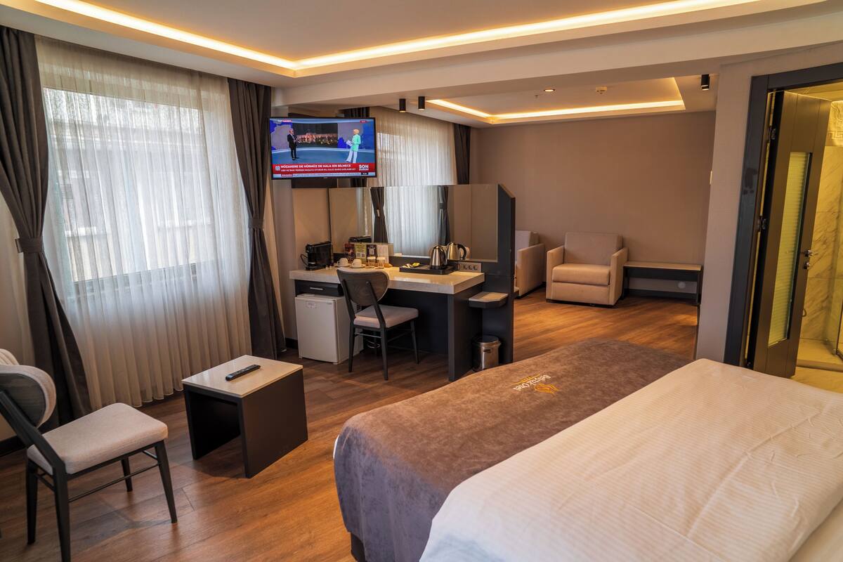 A hotel room with a bed, desk, chair, TV, and curtains.