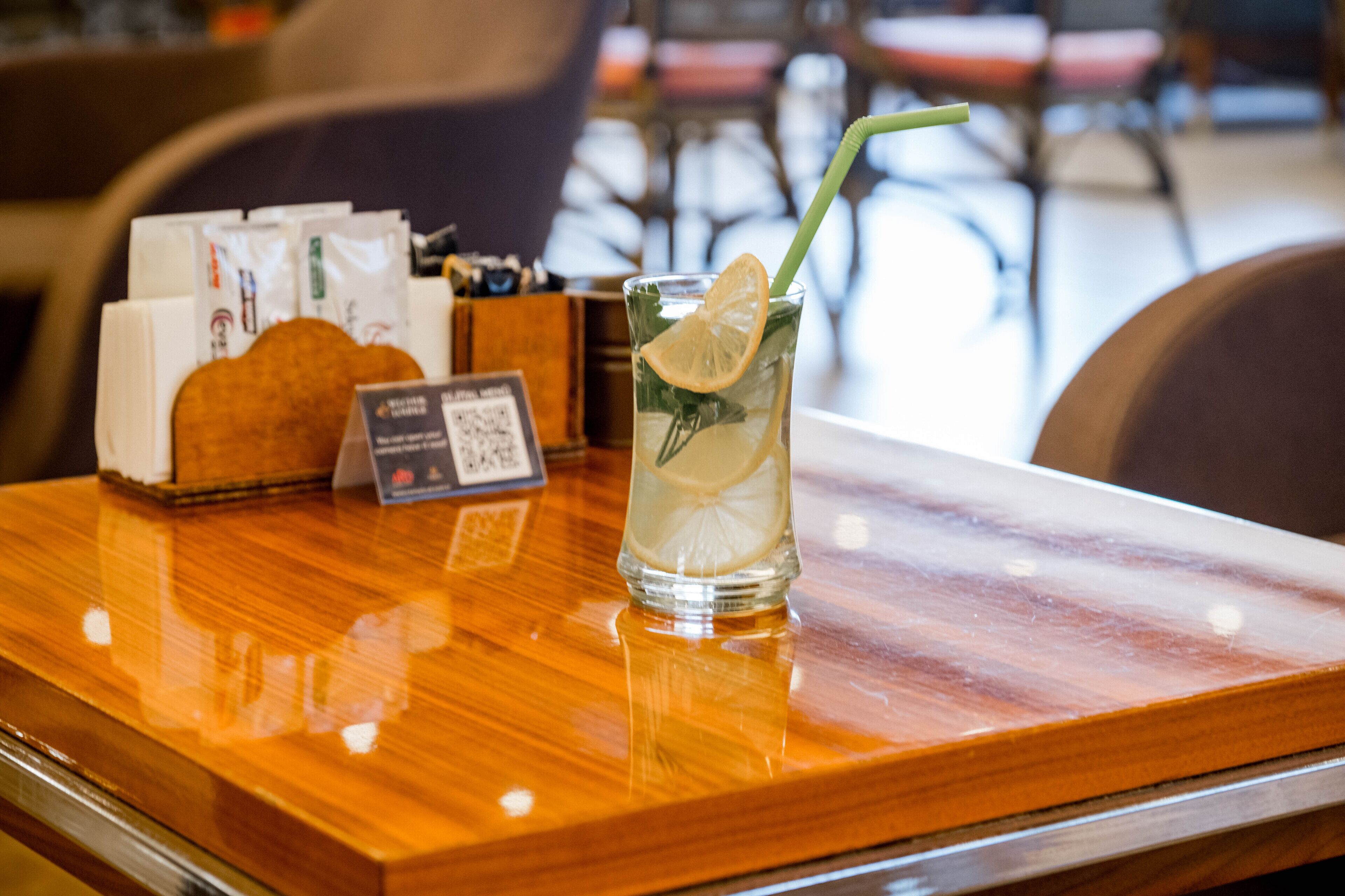 A glass of iced tea with a lemon slice and mint on a wooden table, accompanied by a menu and a small card.