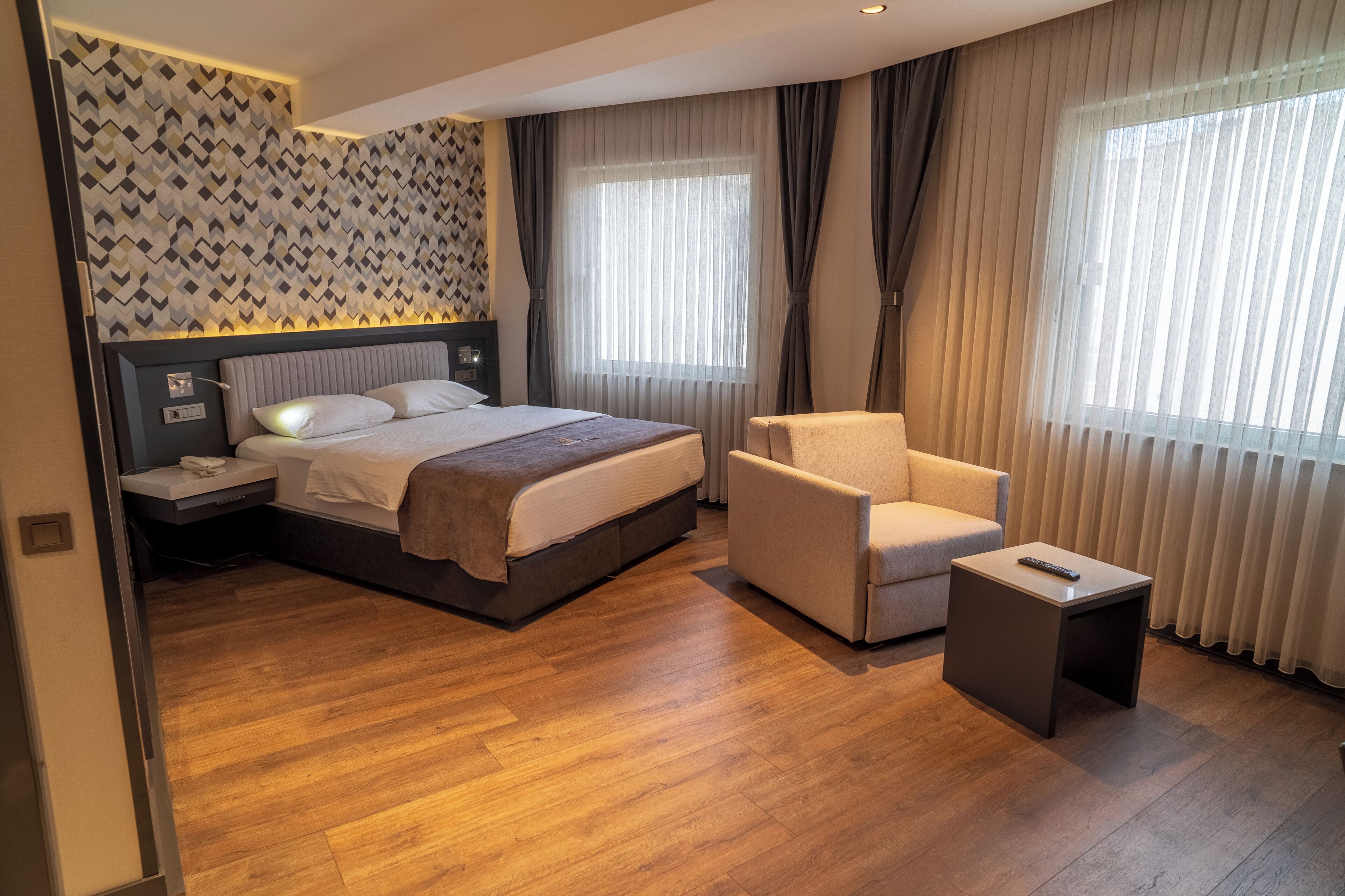 Una habitación de hotel moderna con una cama grande, una mesita de noche, una silla y una pequeña mesita auxiliar.