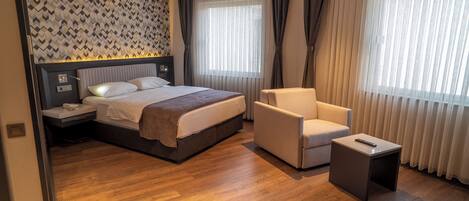 Una habitación de hotel moderna con una cama grande, una mesita de noche, una silla y una pequeña mesita auxiliar.
