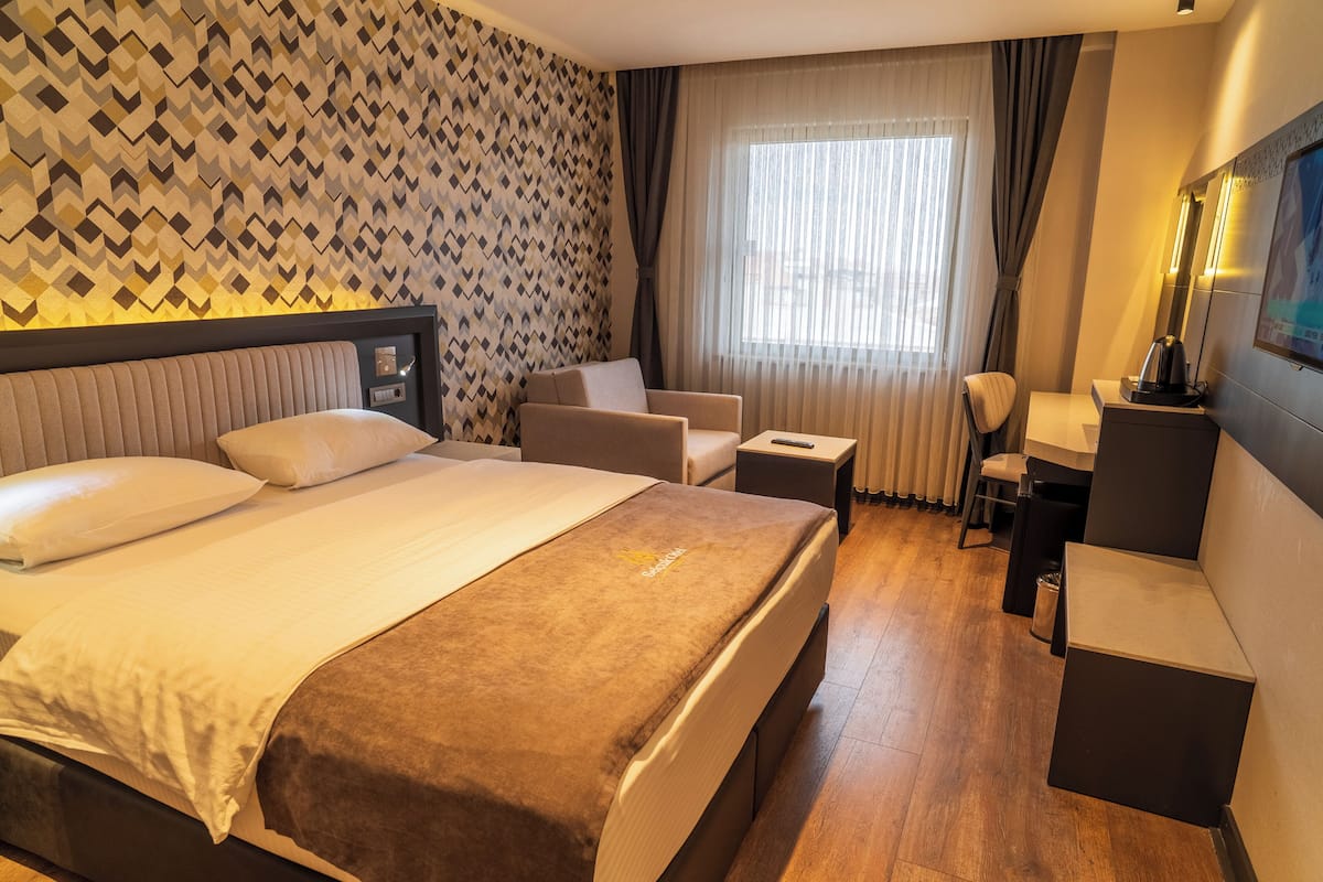 A hotel room with a large bed, a desk, a chair, and a TV.