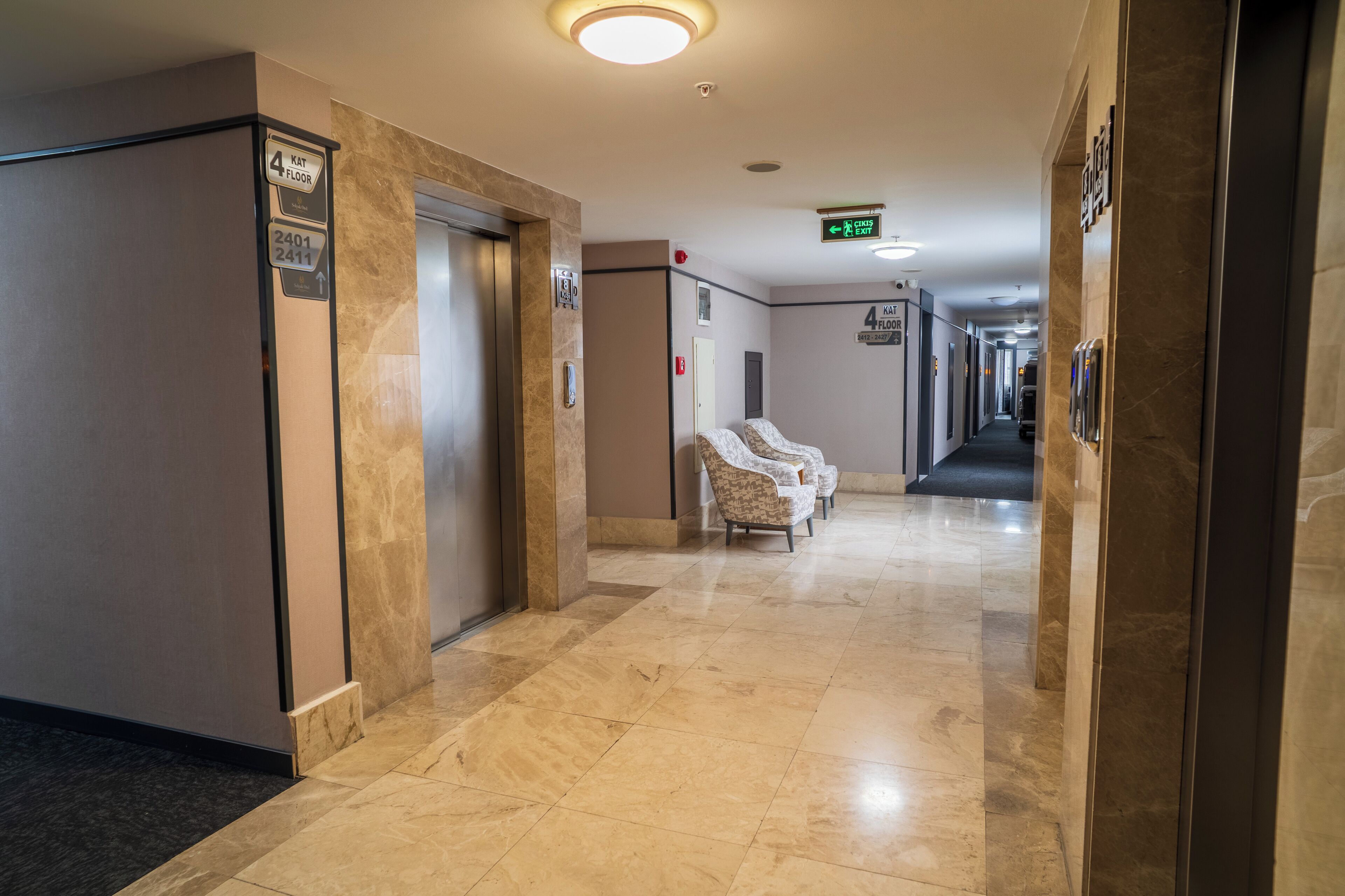 A hotel hallway with a marble floor, a reception desk, and a seating area with chairs.