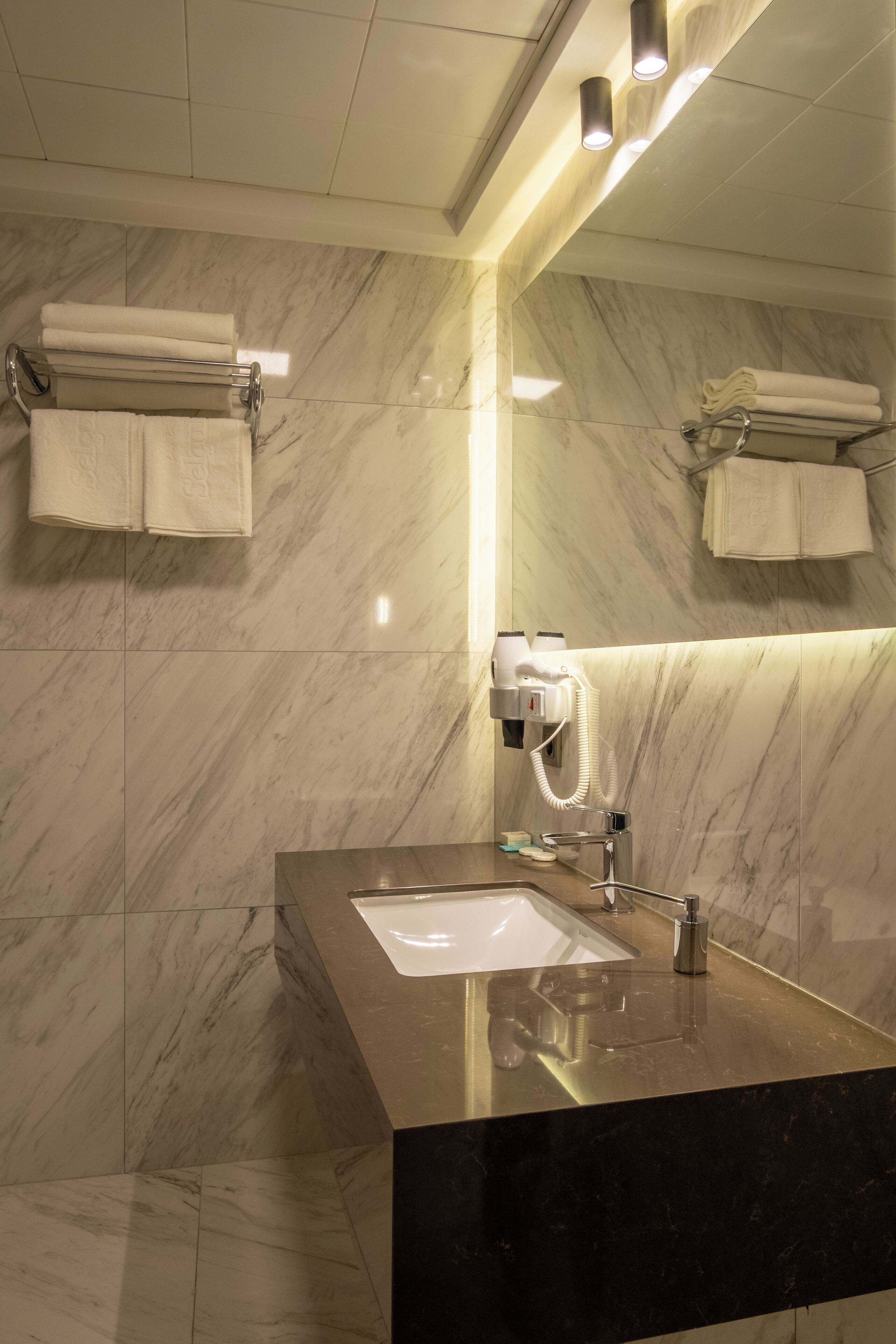 A modern bathroom with a marble floor, a black countertop, a sink, a mirror, and towel racks.
