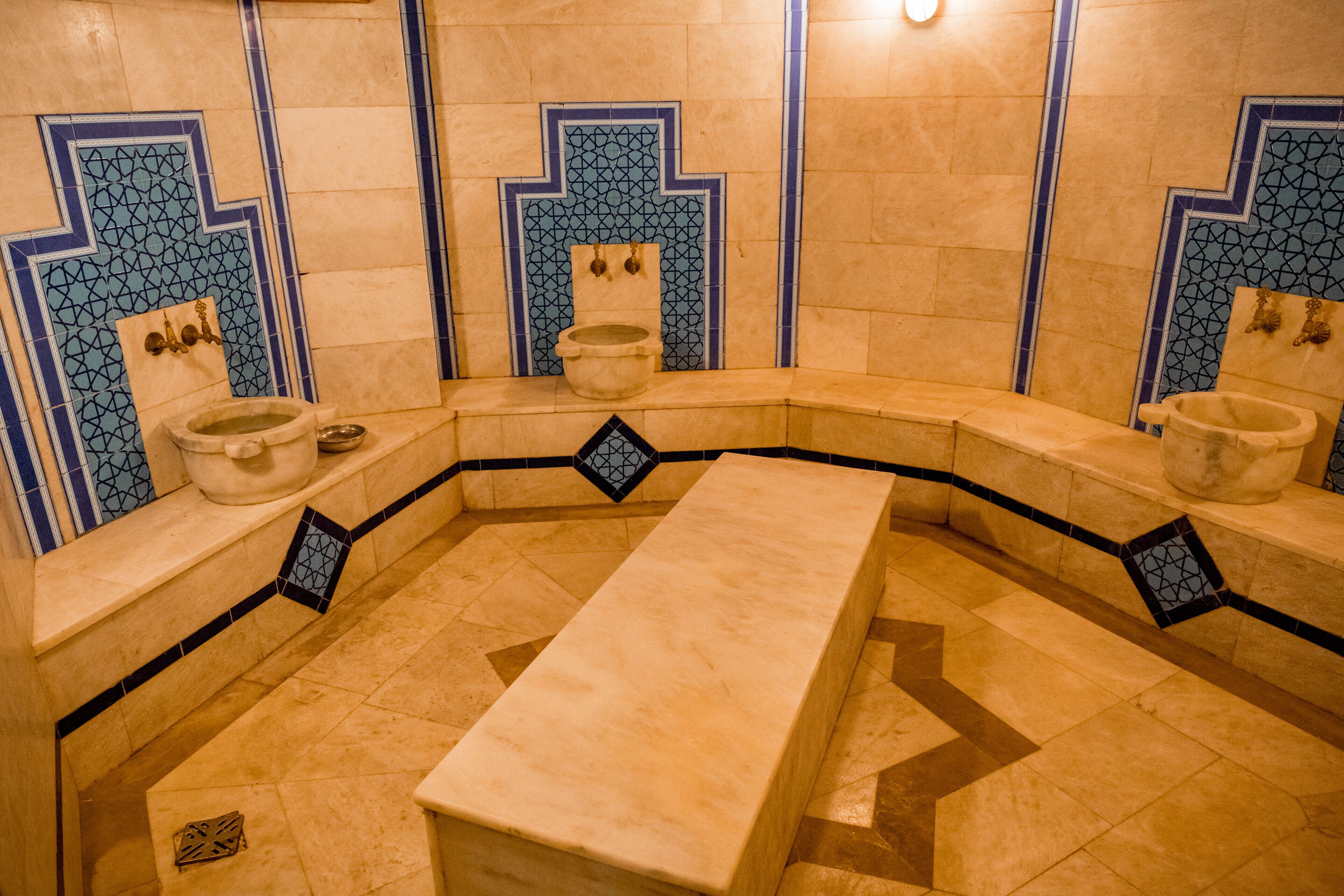 A traditional bathroom with a central bench, two sinks, and decorative blue and beige tiles.