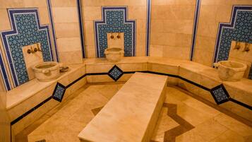 Un baño tradicional con un banco central, dos lavamanos y azulejos decorativos azul y beige.