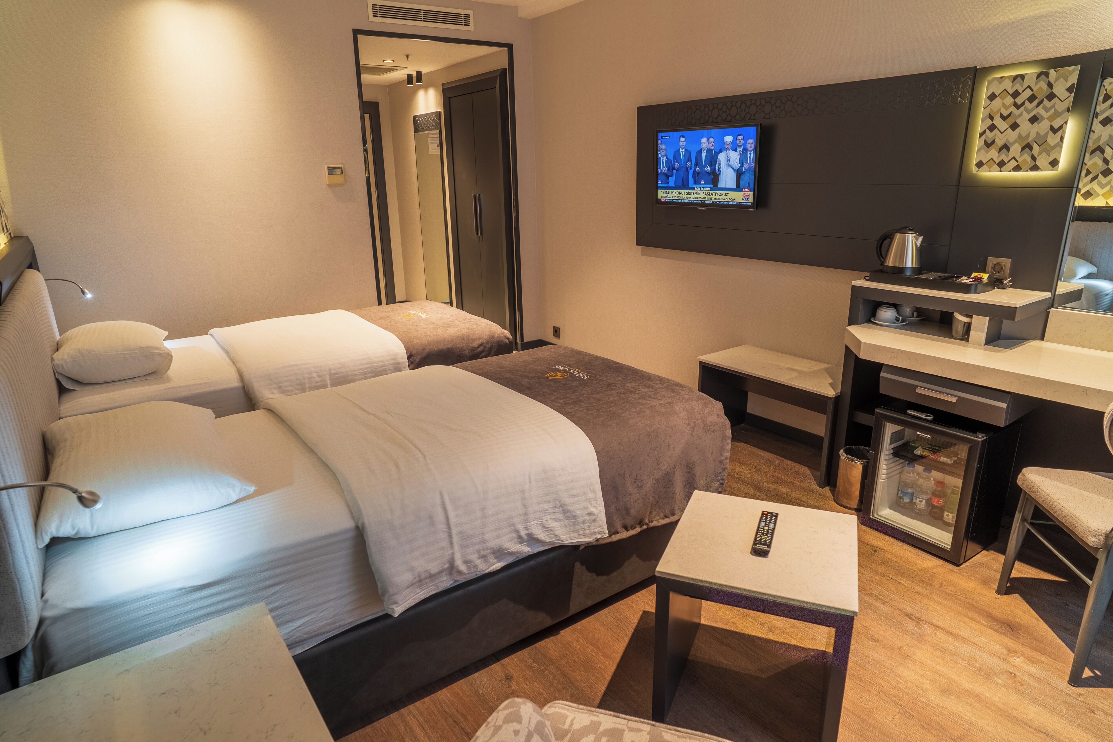 Una habitación de hotel con dos camas, televisión, una mesita y un minibar.