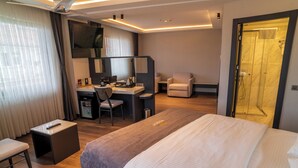 Habitación de hotel con cama, escritorio, silla y zona de ducha.