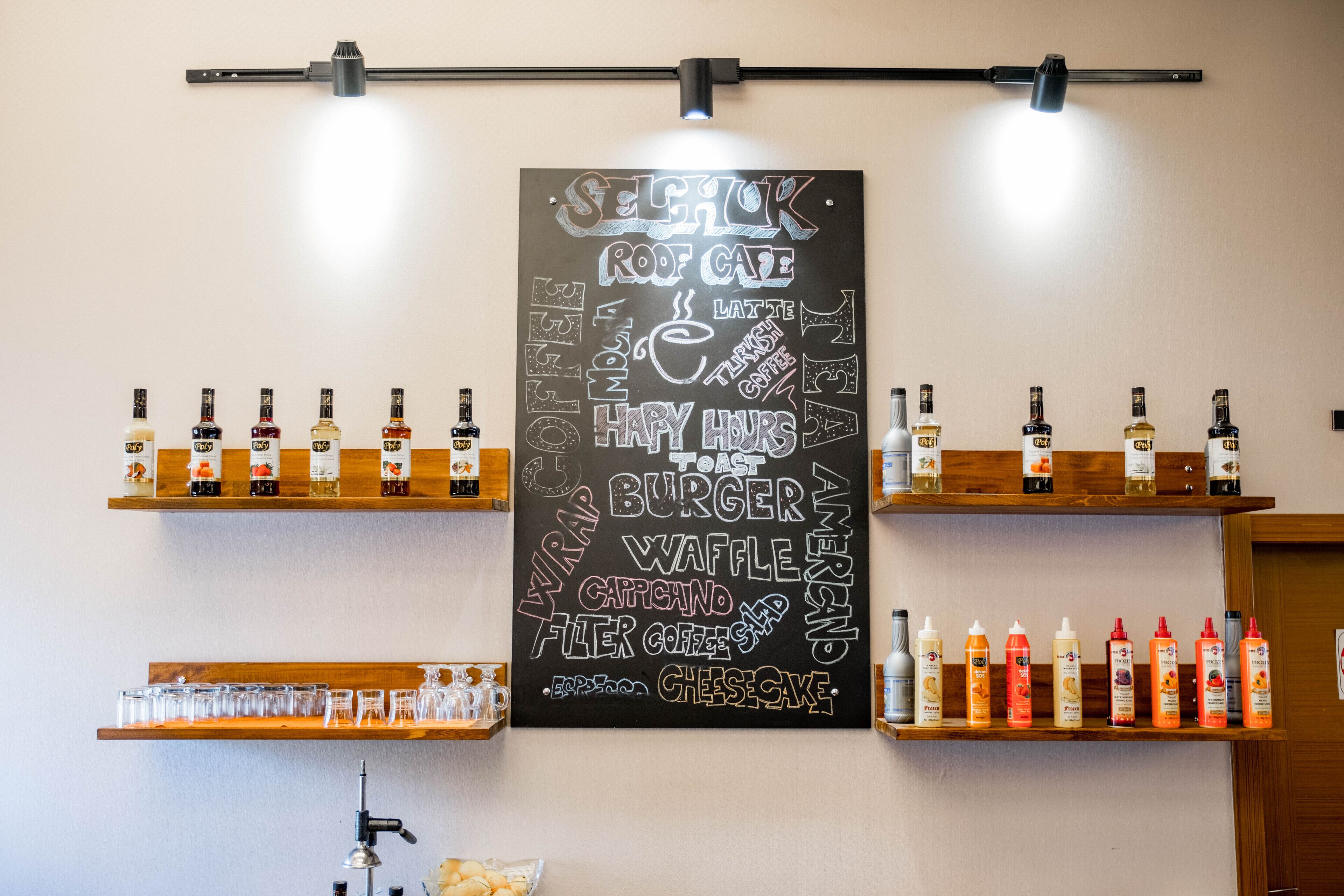 A café with a chalkboard menu listing items like 'roast coffee,' 'latte,' and 'burger.' There are shelves with bottles and glasses.