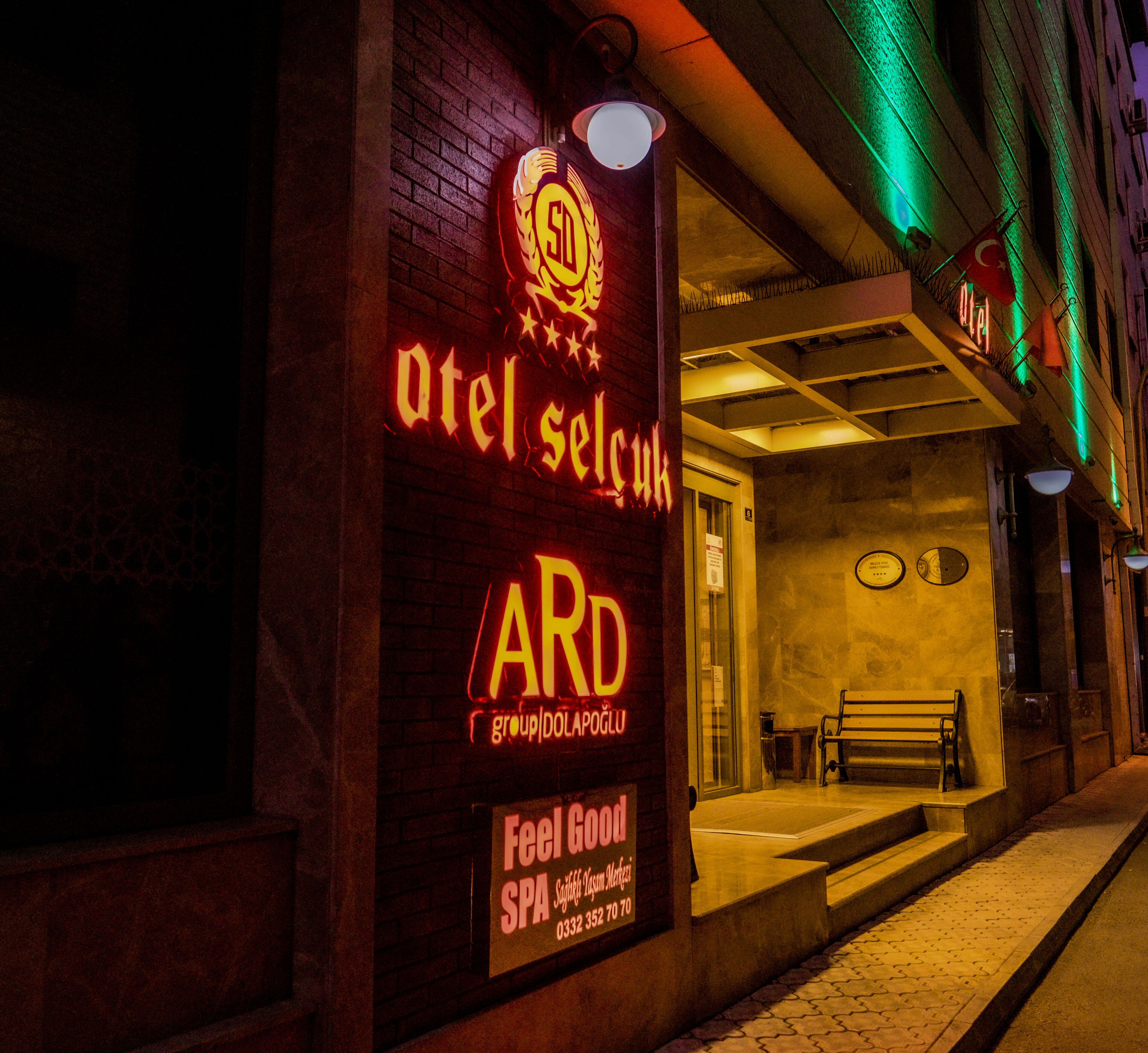 Ein Gebäude mit einer Neonreklame, auf der in leuchtenden Farben "Atel Selcuk" und "ARD" stehen. Vor der Tür befindet sich eine Bank und ein Eingang.