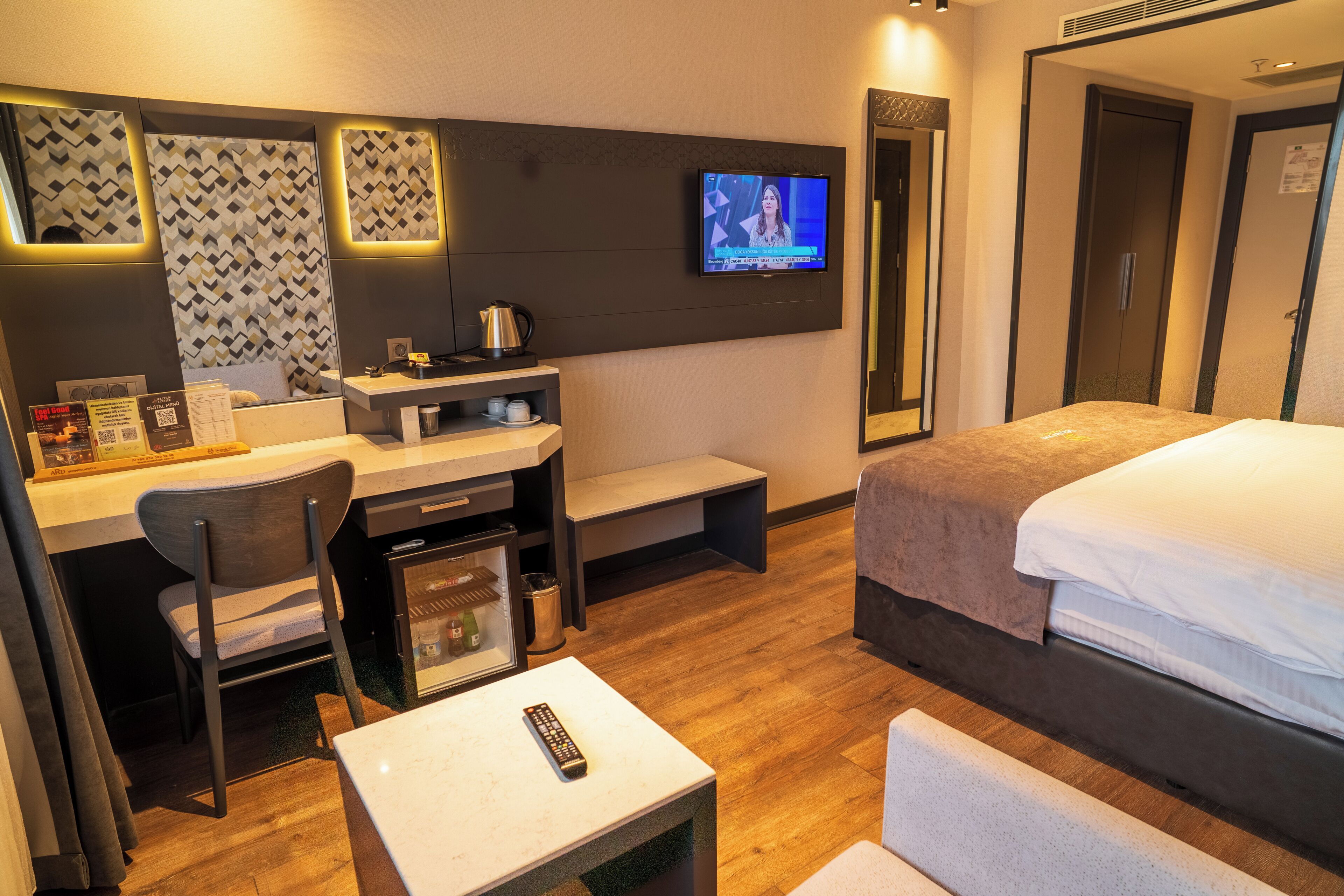 A hotel room with a bed, desk, chair, TV, and a small table with a remote control.