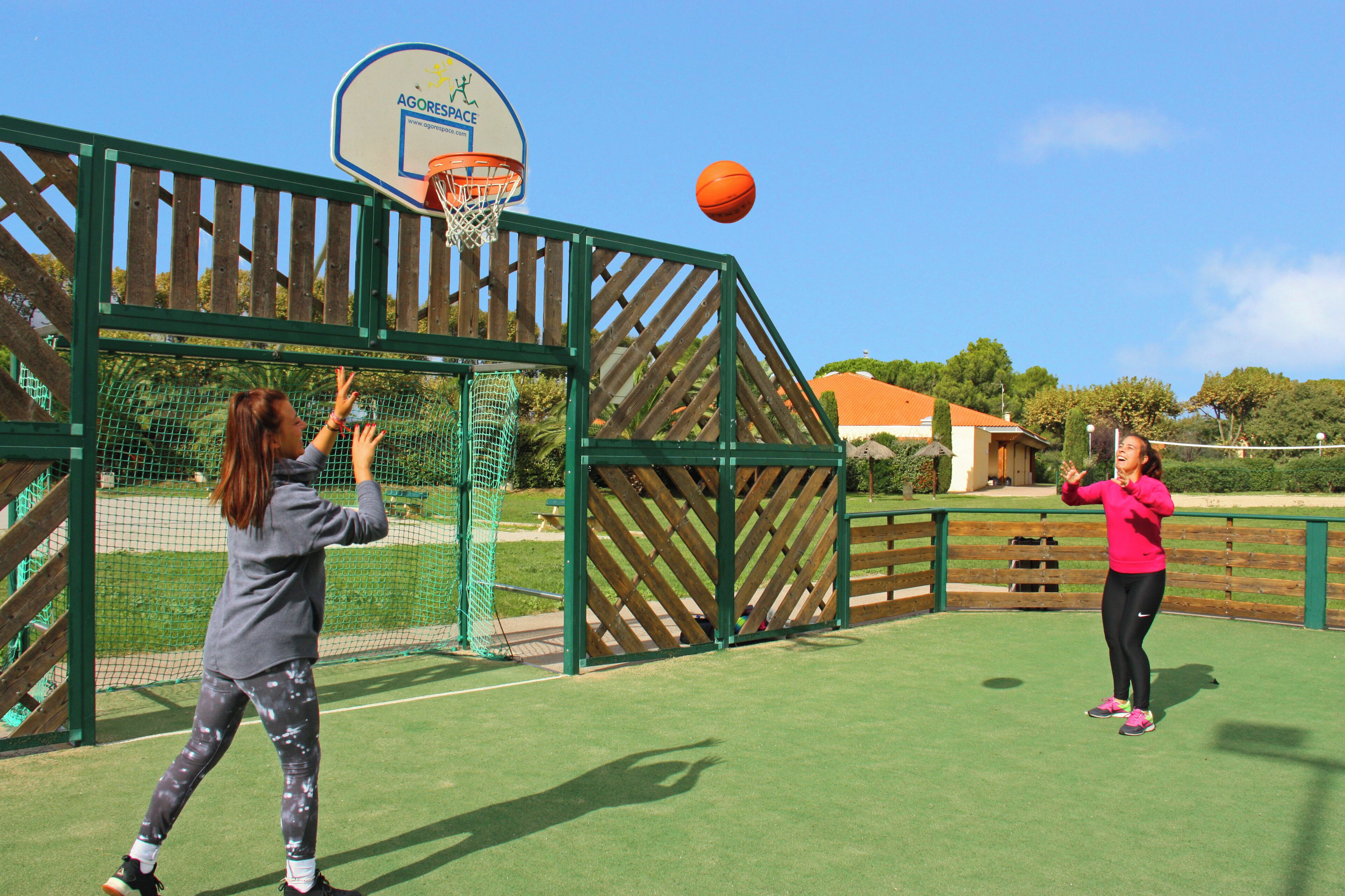Un terrain de basket en plein air, entouré d’une clôture en bois et équipé d’un panier de basket.