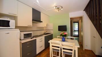 A compact kitchen with white cabinets, a microwave, a stove, and a dining table with chairs.