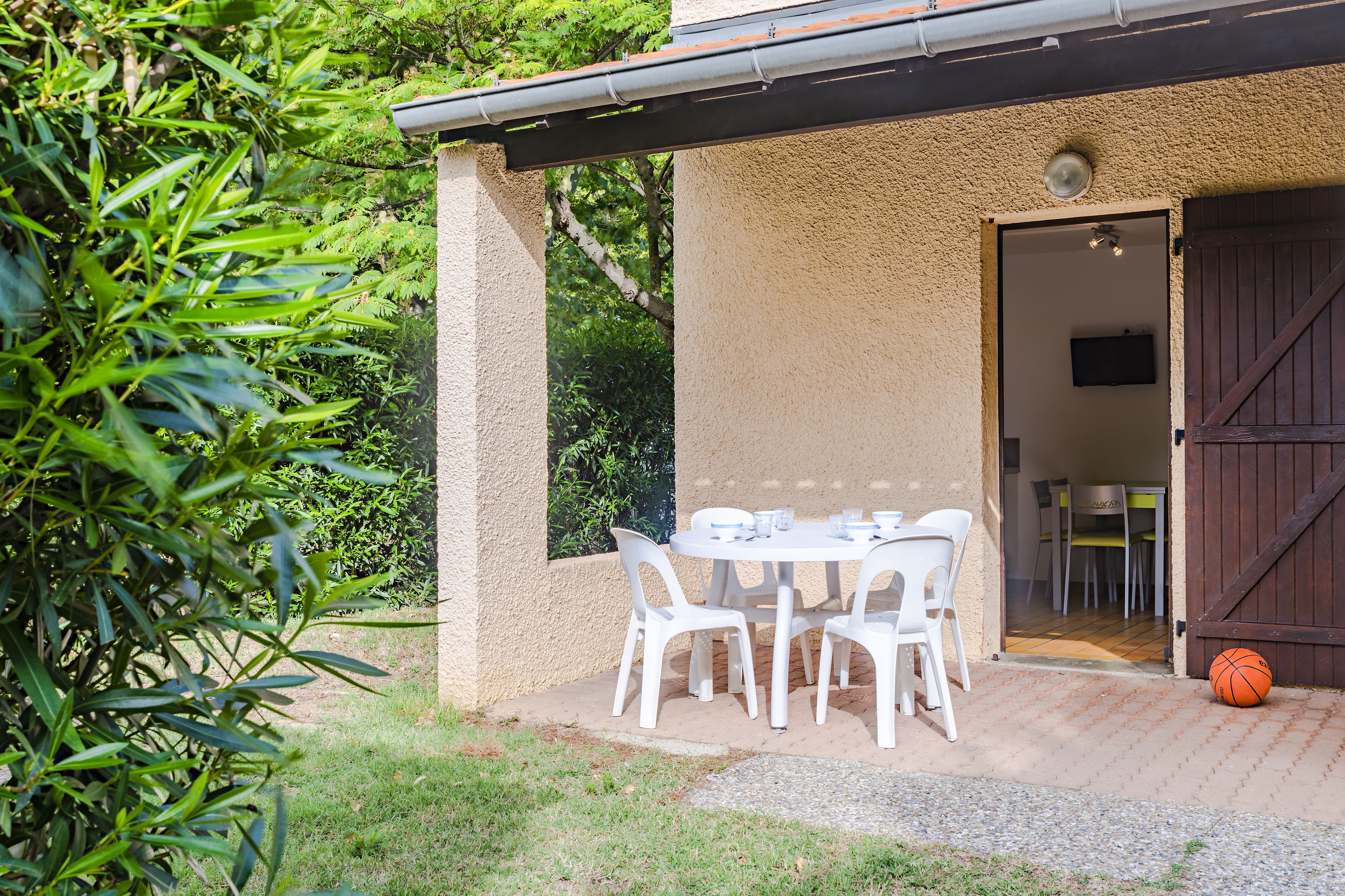 Une terrasse extérieure avec une table et des chaises, une porte donnant sur l’intérieur et un ballon de basket-ball par terre.