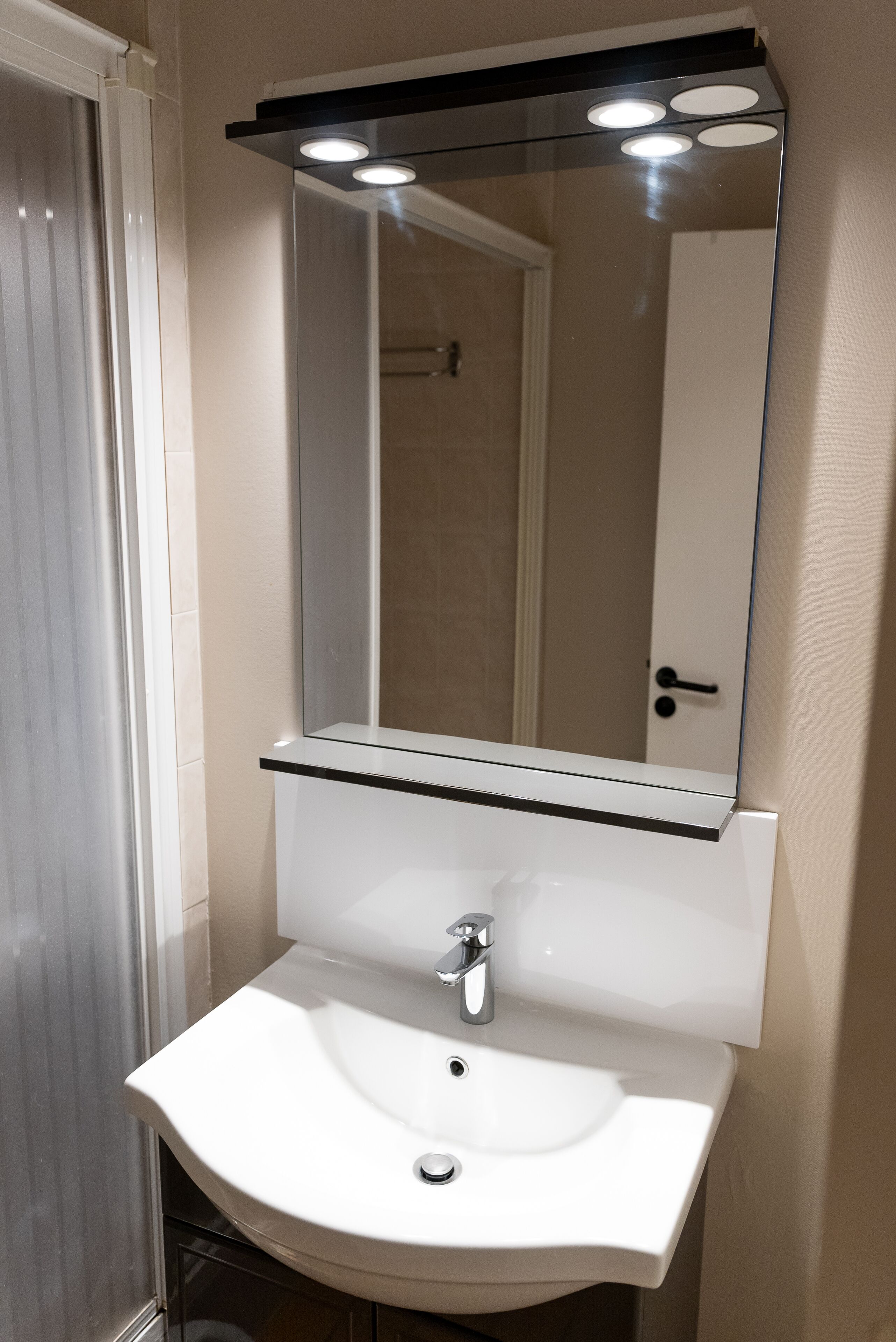 Un baño con un lavamanos blanco, un espejo y una puerta.