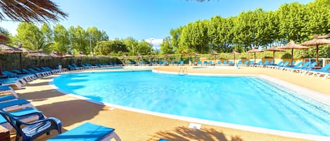 A swimming pool with blue lounge chairs and thatched umbrellas.