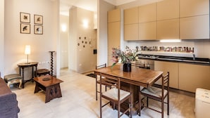 Cozinha moderna com armários de madeira, uma mesa de jantar com cadeiras e uma pequena mesa lateral com uma luminária.