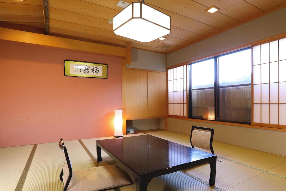 Una habitación tradicional japonesa con suelo de tatami, una mesa baja, un cojín y una lámpara colgante.