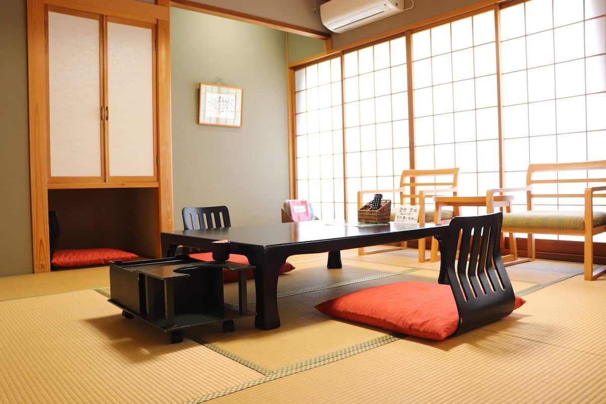 Una habitación con esterillas de tatami, una mesa baja, sillas y un armario.