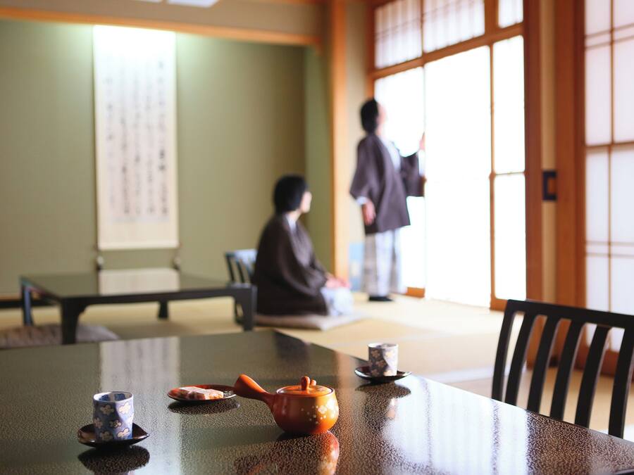 A traditional Japanese room with tatami flooring, a low table with tea set, and a sliding door.
