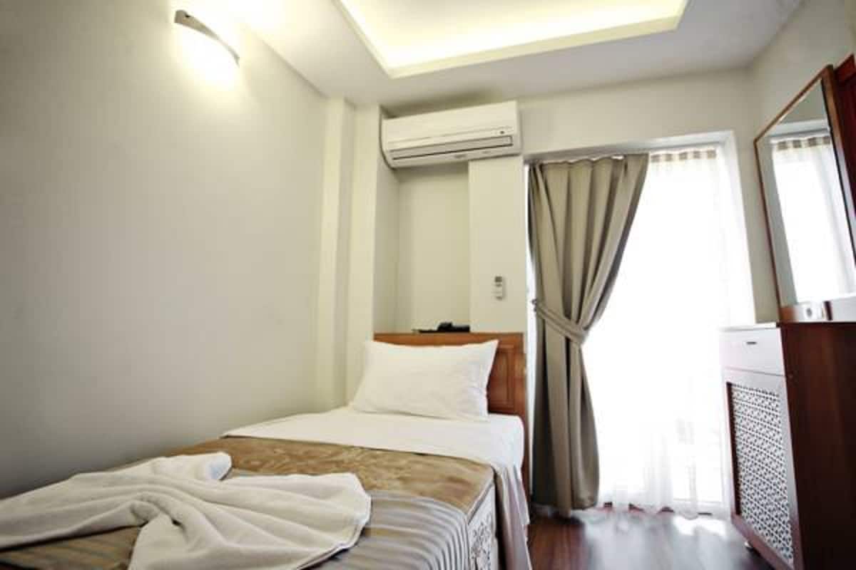 A hotel room with a bed, an air conditioning unit, a window with curtains, and a radiator.