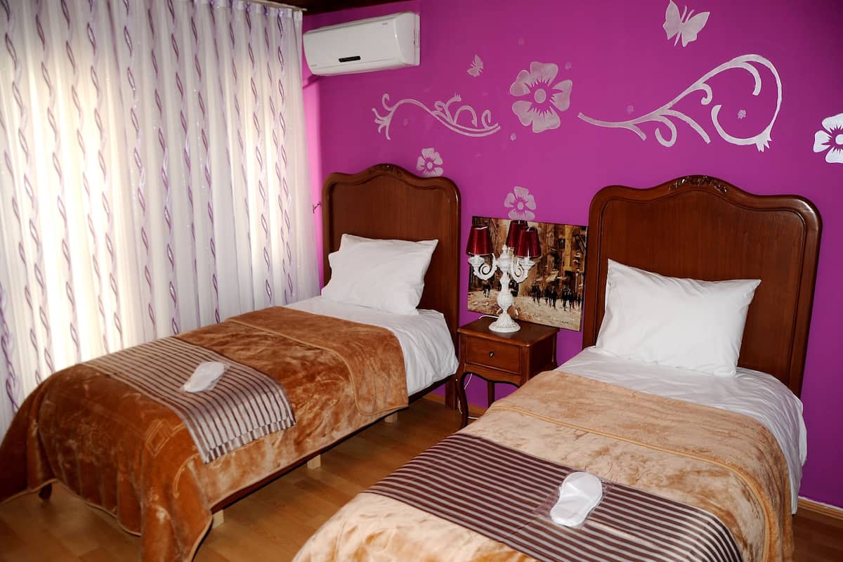 A hotel room with two beds, a nightstand, a lamp, and a wall with floral decals.