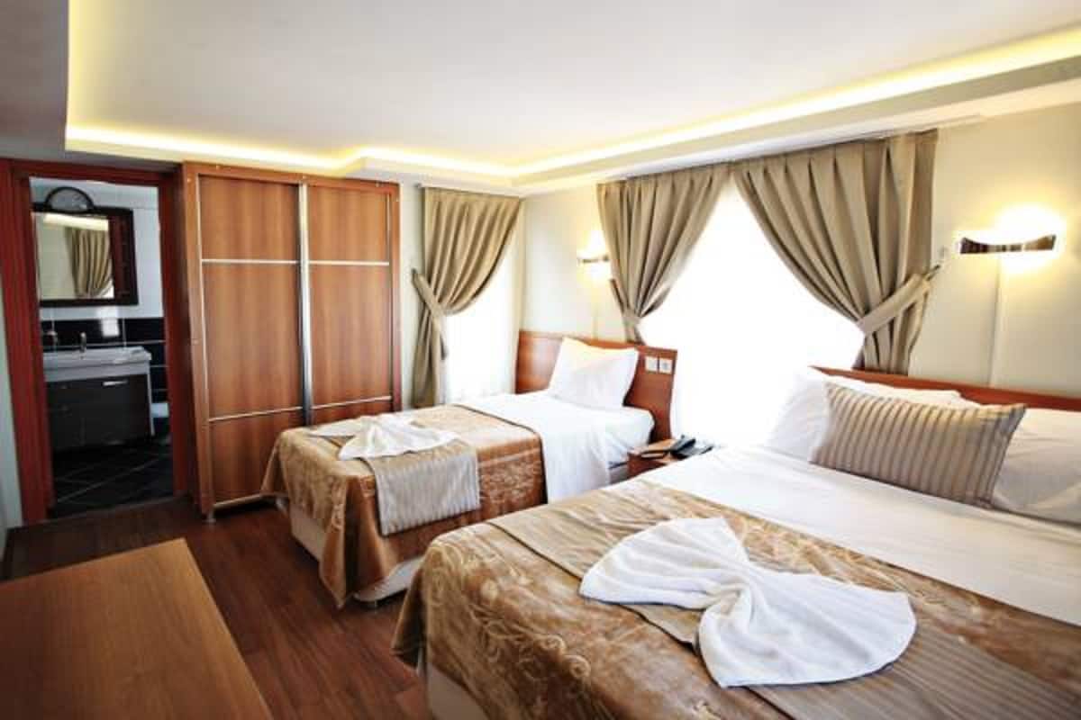 A hotel room with two beds, a wooden wardrobe, a bathroom with a mirror, and beige curtains.