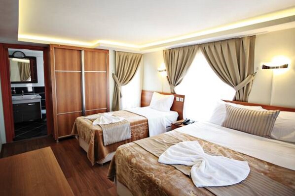 Ein Hotelzimmer mit zwei Betten, einem Holzschrank, einem Badezimmer mit Spiegel und beige farbenen Vorhängen.
