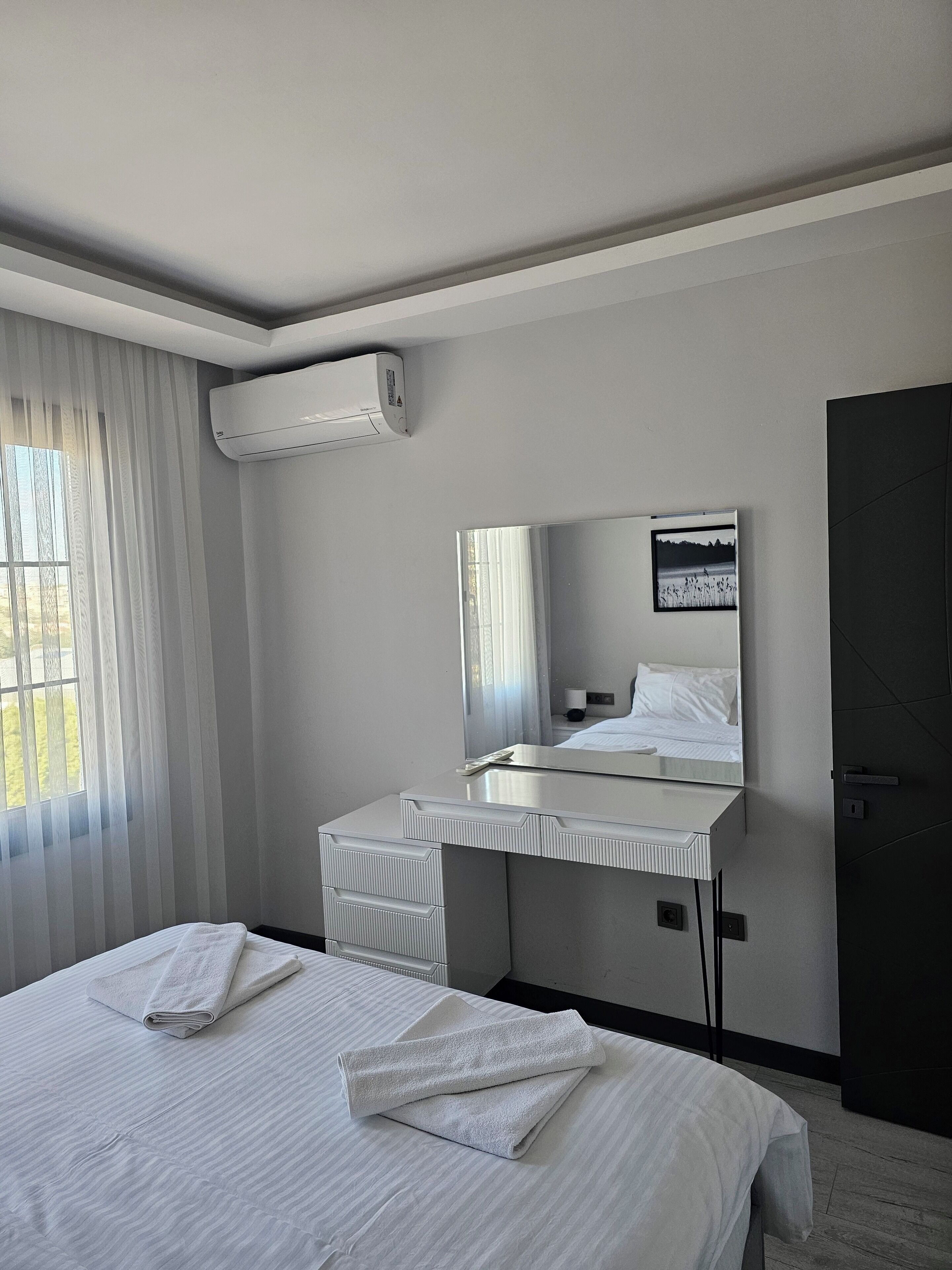Habitació d'hotel amb un llit, una taula de treball, un mirall i un aire condicionat.