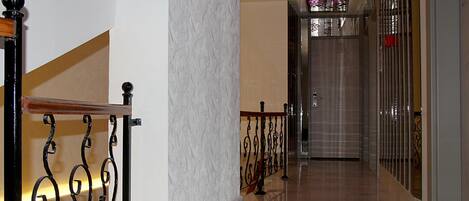 Un pasillo con piso de mármol, barandilla de metal y una puerta con panel de vidrio.