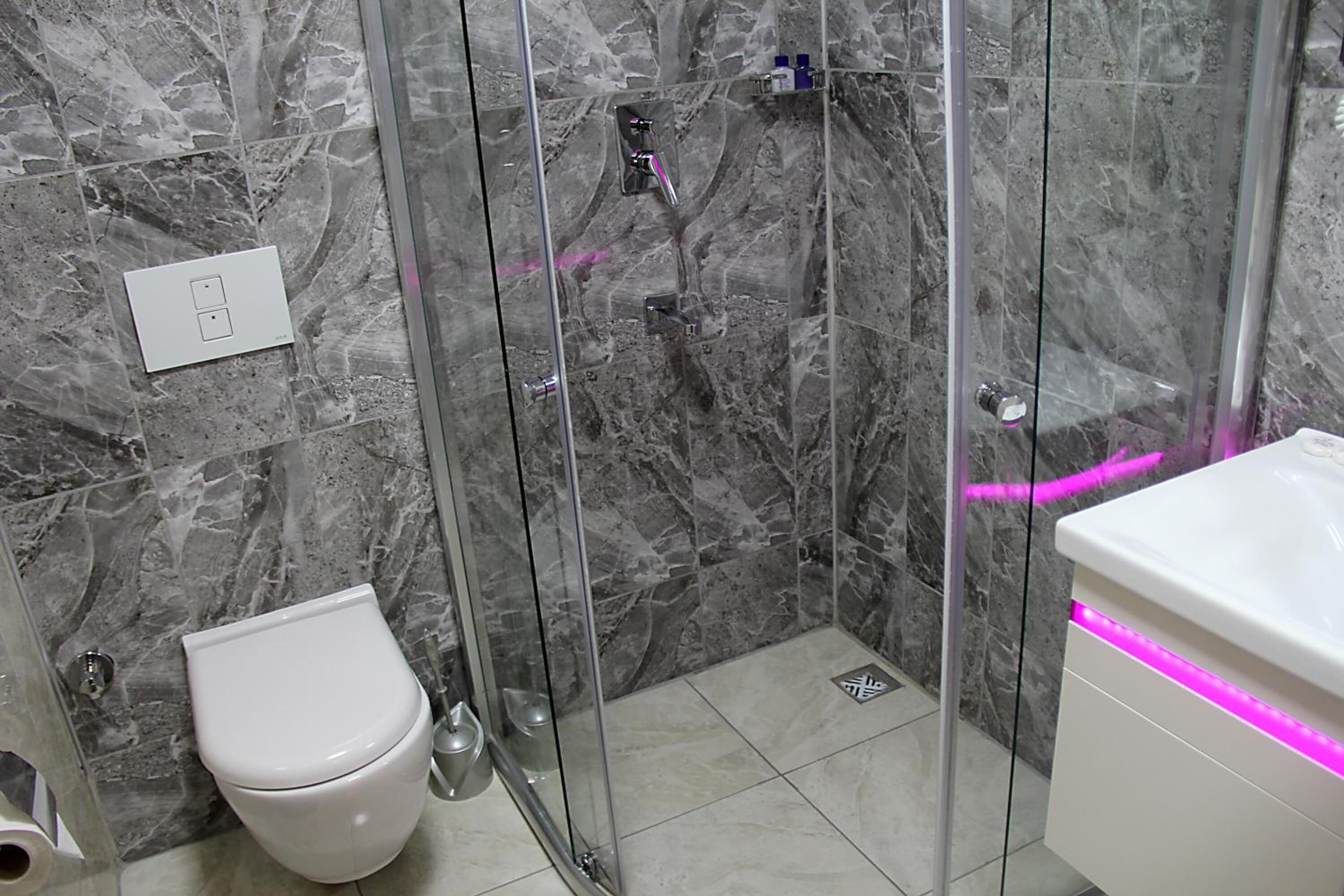 Une salle de bain avec une douche à parois de verre, des toilettes blanches et un lavabo doté d’un éclairage LED rose.