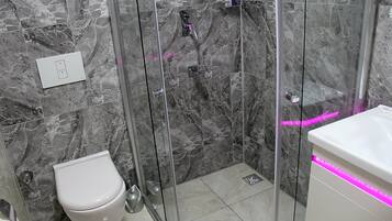 Une salle de bain avec une douche à parois de verre, des toilettes blanches et un lavabo doté d’un éclairage LED rose.