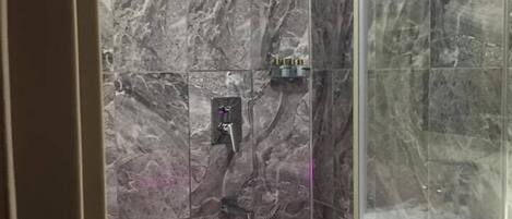 A bathroom with marble walls and a glass shower enclosure.