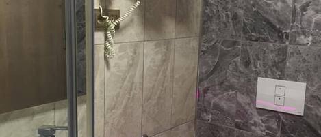Un baño con cabina de ducha de vidrio, un lavabo blanco, un inodoro y una pared de mármol.