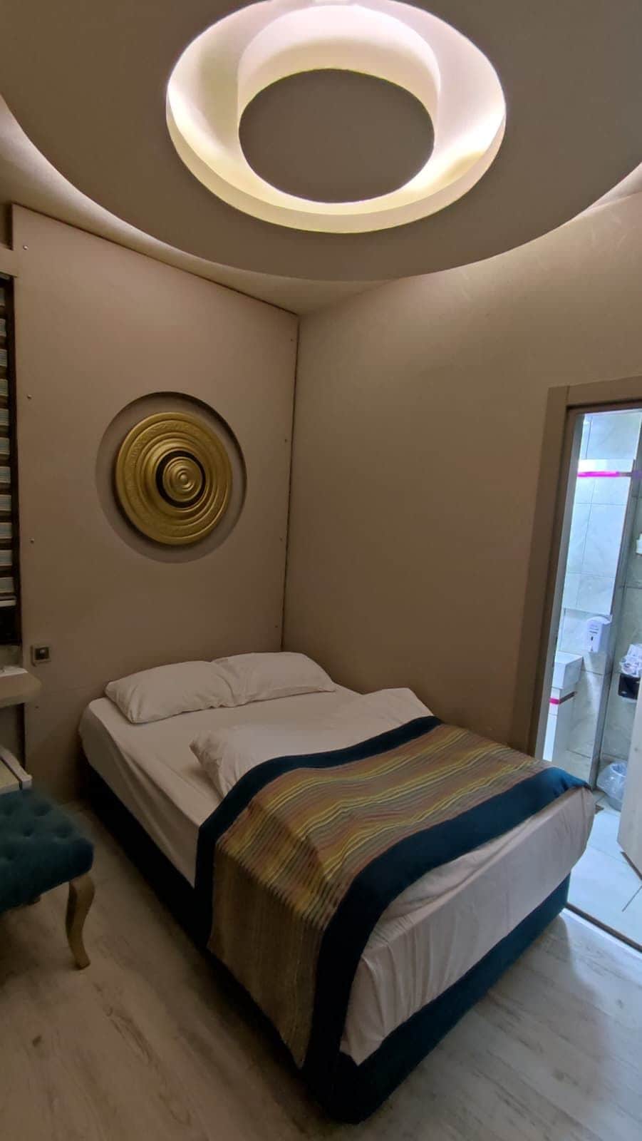 Un dormitorio moderno con cama, lámpara de techo circular y un pequeño adorno redondo en la pared.