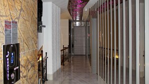 A hallway with a marble wall, a digital elevator display, and a patterned ceiling. - Nun Otel (Konya)