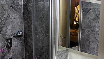A modern bathroom with a glass-enclosed shower, a white sink, and marble walls.