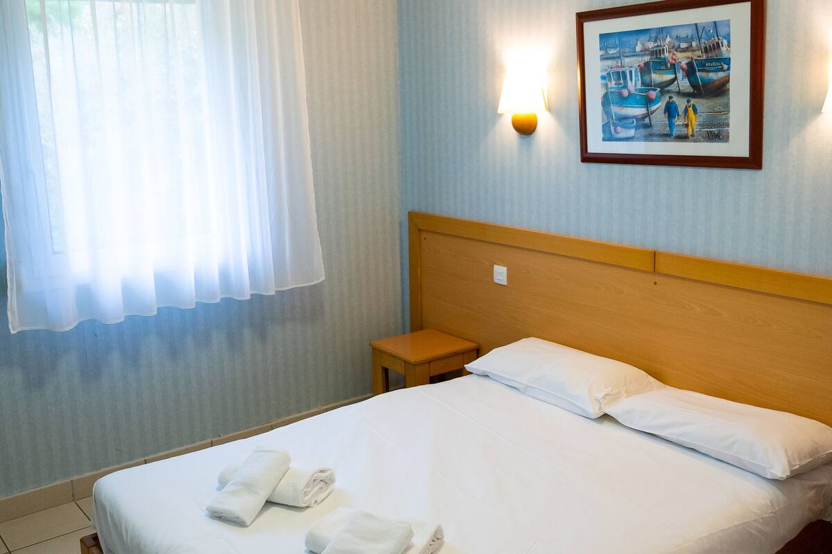 A hotel room with a neatly made bed, a bedside table, a lamp, and a painting on the wall.