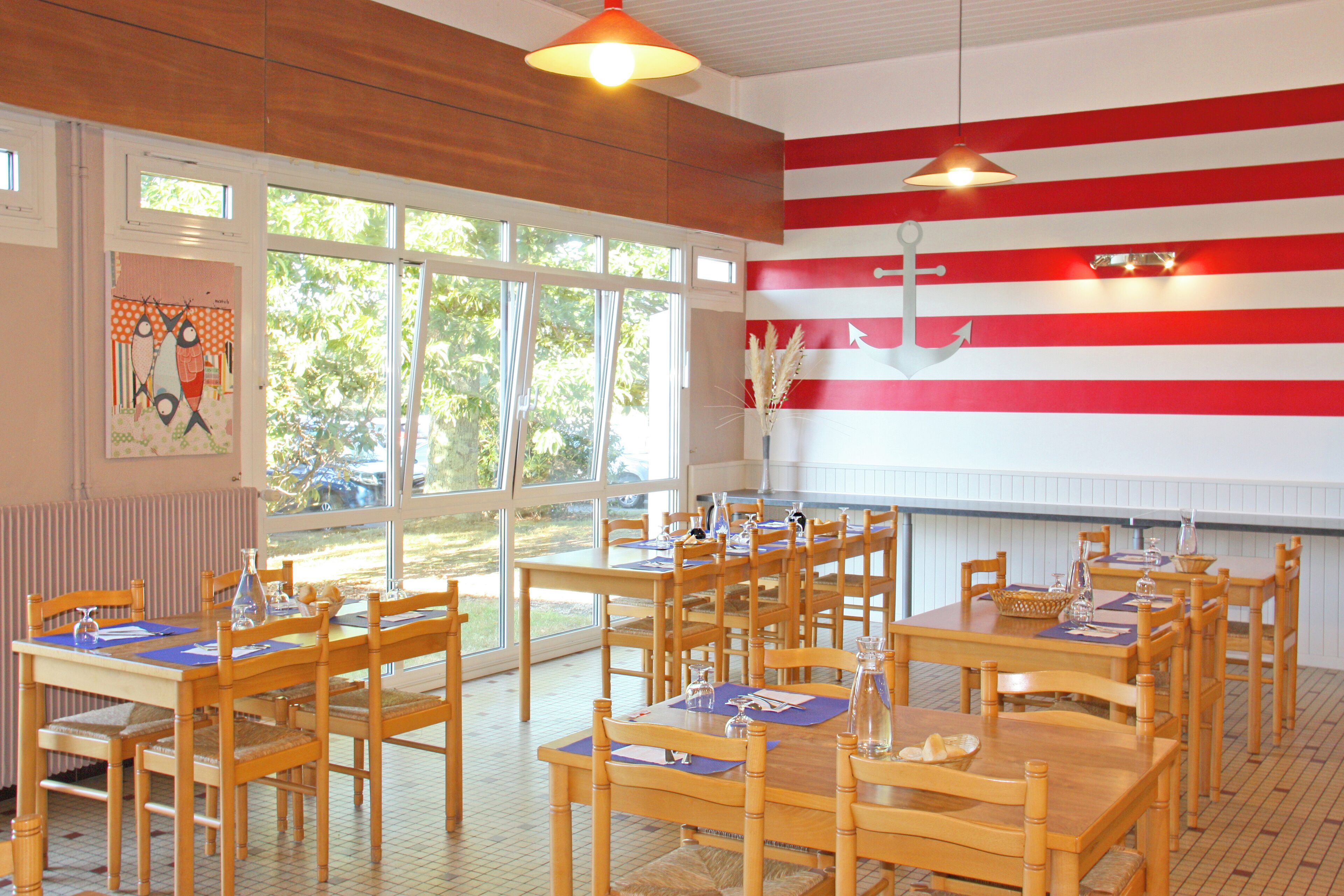 A dining area with wooden tables and chairs, large windows, and a wall with red and white stripes.