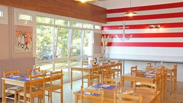 A dining area with wooden tables and chairs, large windows, and a wall with red and white stripes.
