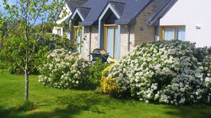 A two-story house with a stone facade, a dark roof, and a well-maintained garden with white flowering bushes. - Azureva Tregunc (Tregunc)